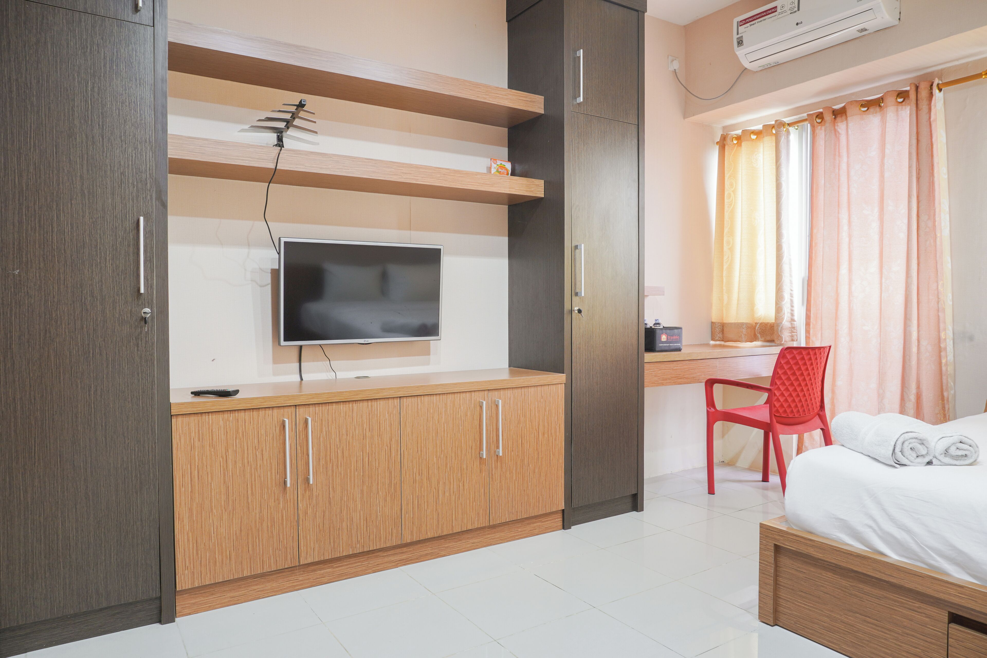 A modern hotel room with a flat-screen TV, wooden cabinets, a desk with a chair, and a bed with neatly folded towels.