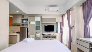 A hotel room with a bed, a TV, a desk, and a kitchenette. - Minimalist Studio At Margonda Residence 3 Apartment (Depok)