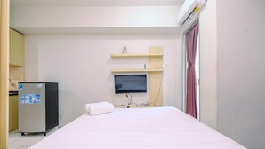 Een hotelkamer met een bed, een aan de muur bevestigde televisie, een klein schap erboven en een koelkast aan de linkerkant.