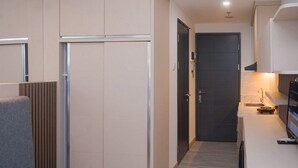 A modern kitchen with a dark door, a grey chair, and a small countertop with a sink. - Fancy And Homey Studio Room At Collins Boulevard Apartment (Tangerang)