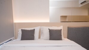 A neatly made bed with white and gray bedding, a headboard with a light fixture, and a built-in shelf above the bed. - Fancy And Homey Studio Room At Collins Boulevard Apartment (Tangerang)