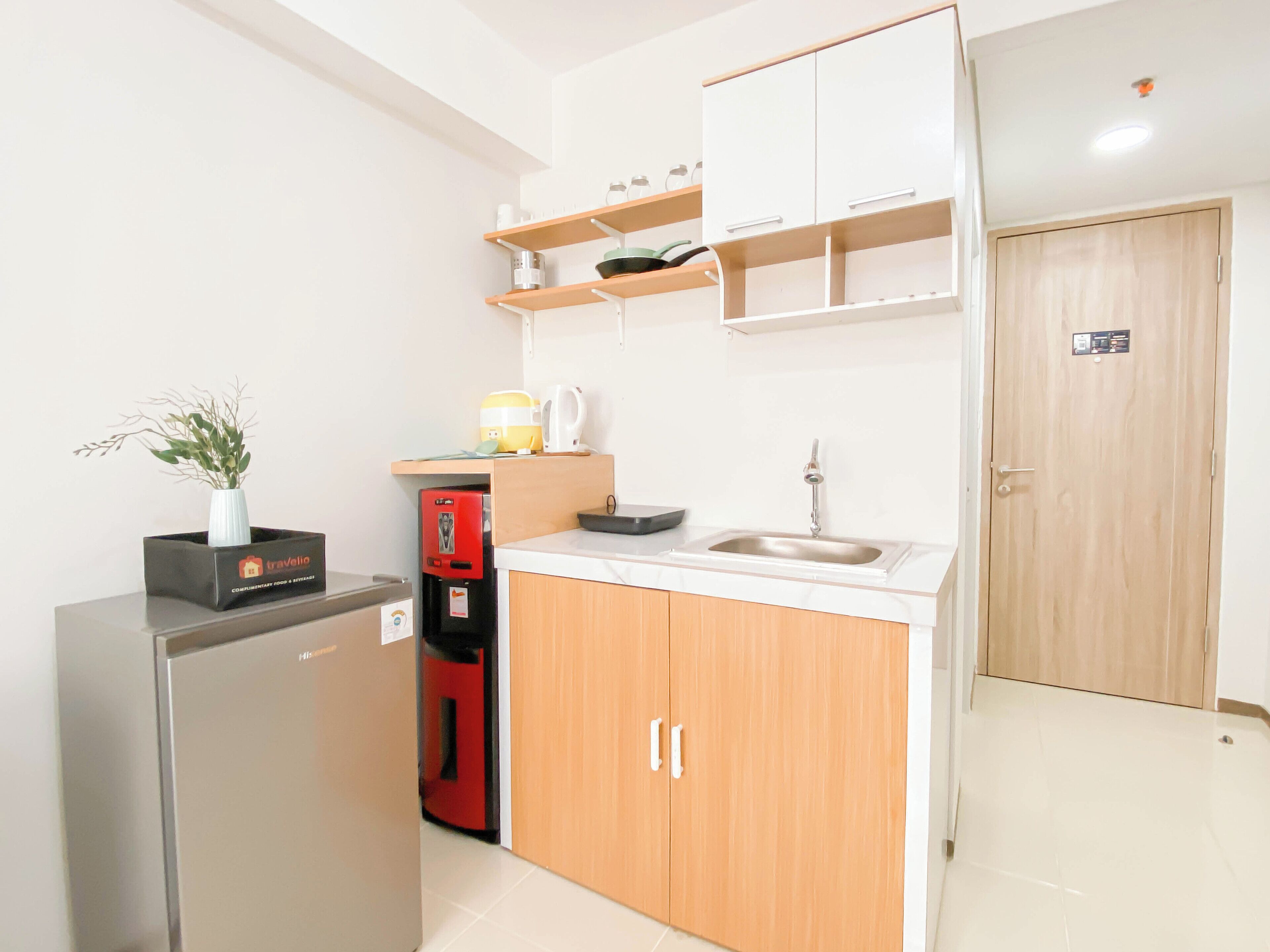 A compact kitchen with a refrigerator, a coffee machine, a sink, and wooden cabinets.