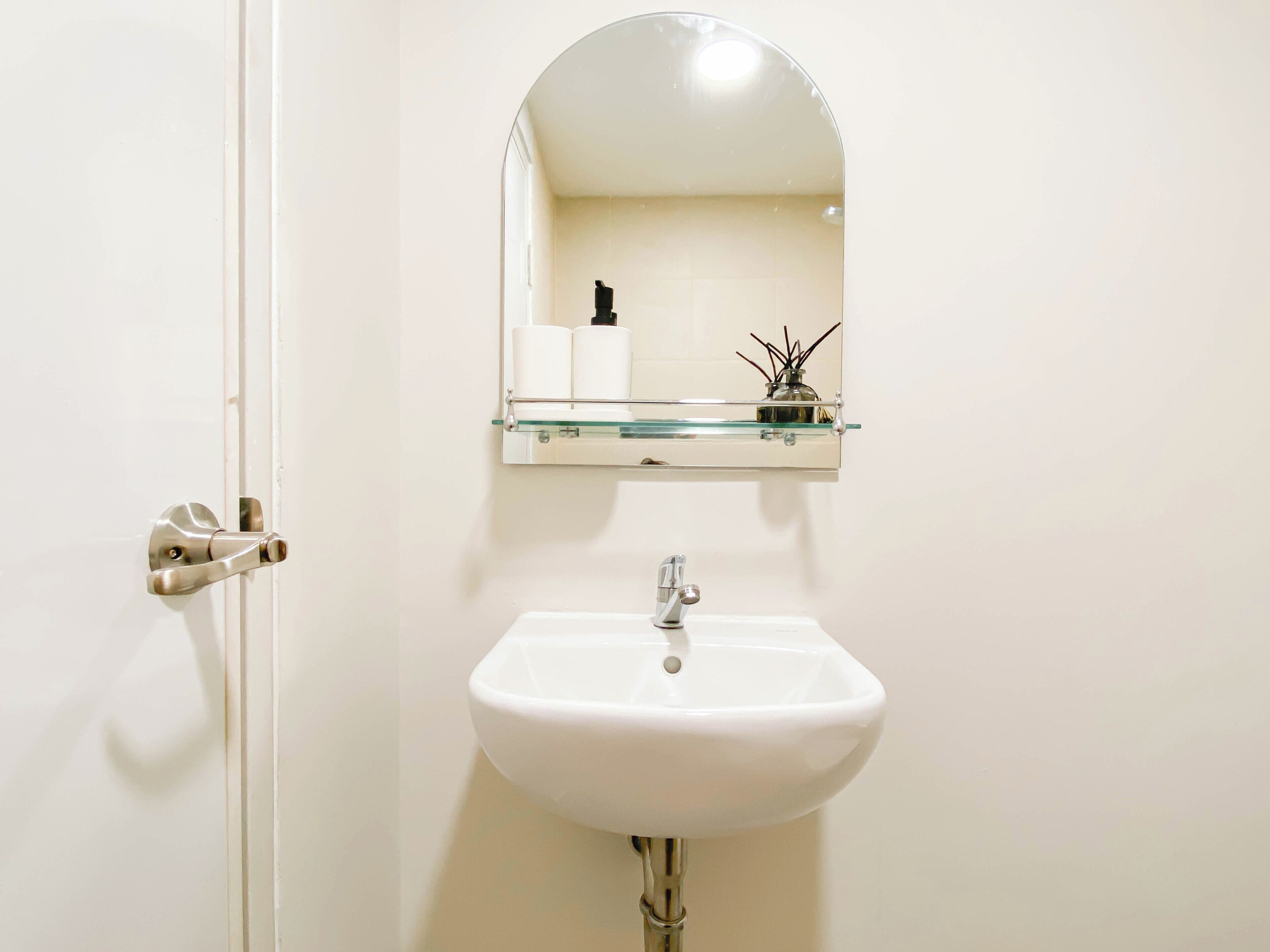 Un baño con un lavabo blanco, un estante de cristal encima y un espejo.