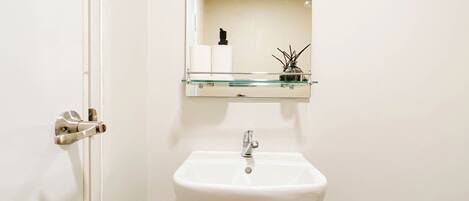 Un baño con un lavabo blanco, un estante de cristal encima y un espejo.