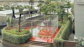 A basketball court surrounded by a metal fence, with steps leading up to it.