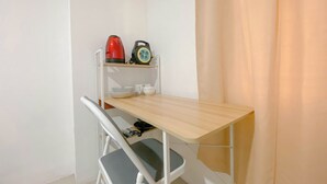 Een compacte, netjes ingerichte kamer met een houten bureau, een stoel, een plankje met een waterkoker en een radio, en een gordijn.