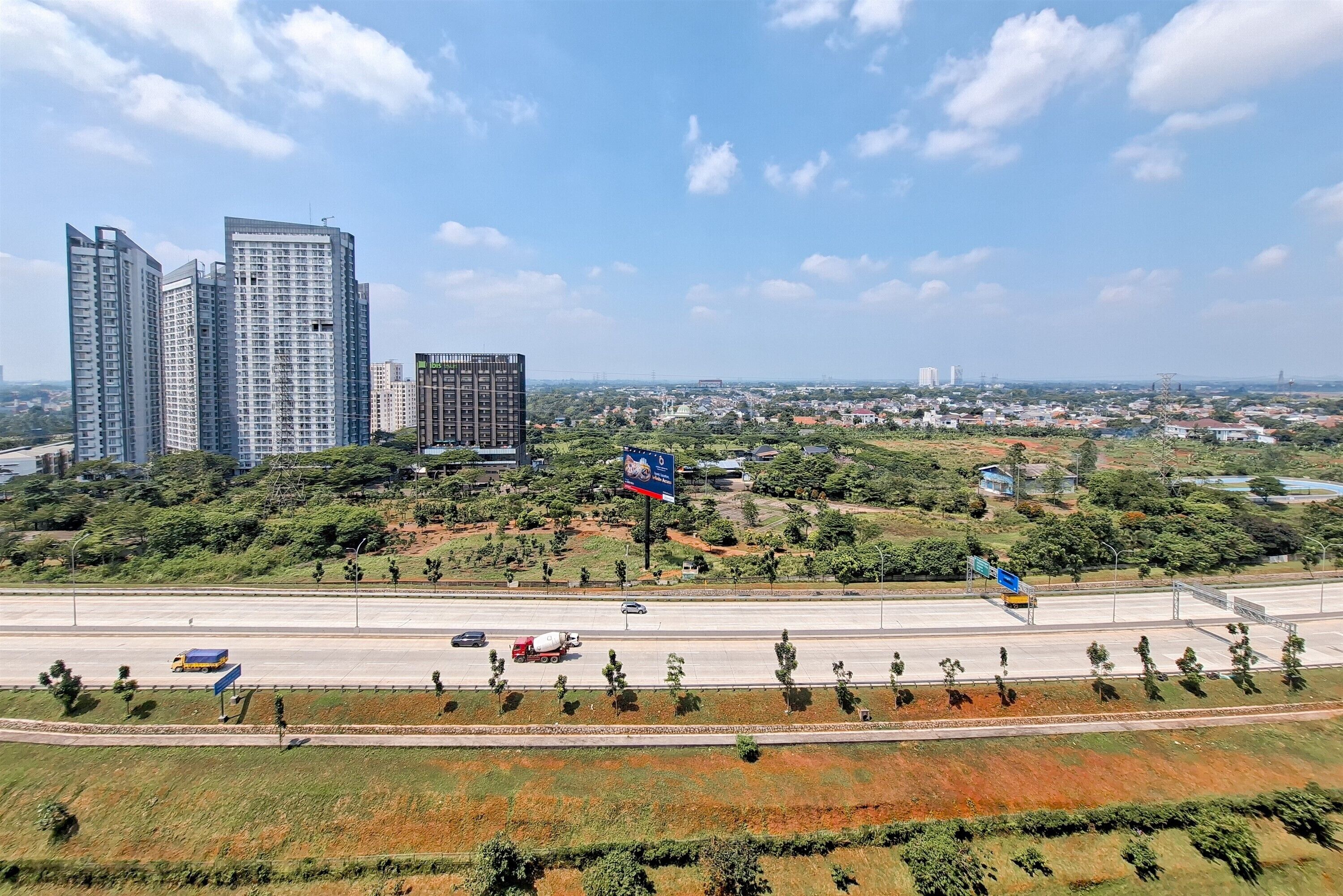 A cityscape with modern high-rise buildings, a highway, and a mix of greenery and urban development.