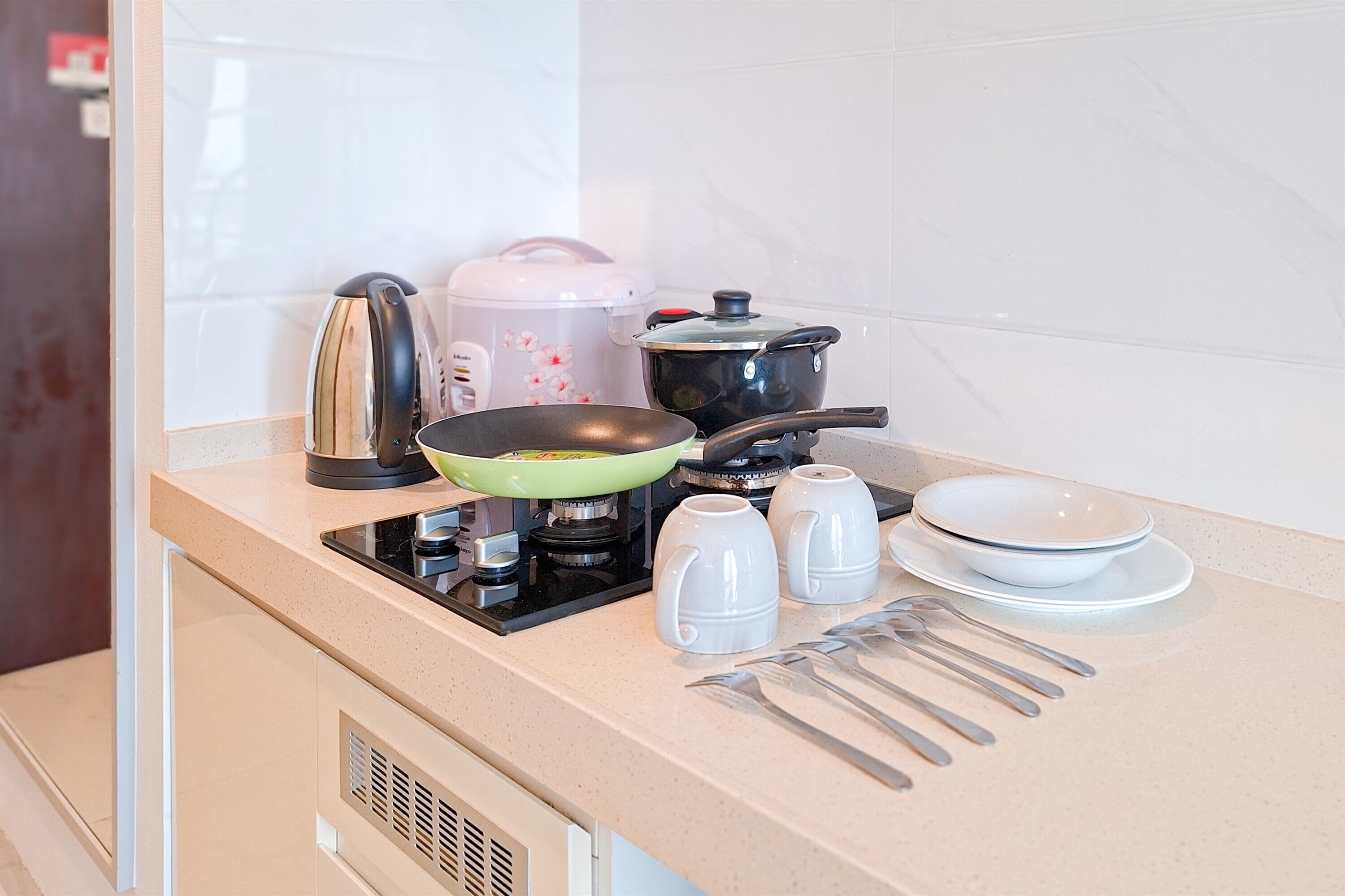 A kitchen with a stove, a frying pan, a kettle, a rice cooker, and a pot.