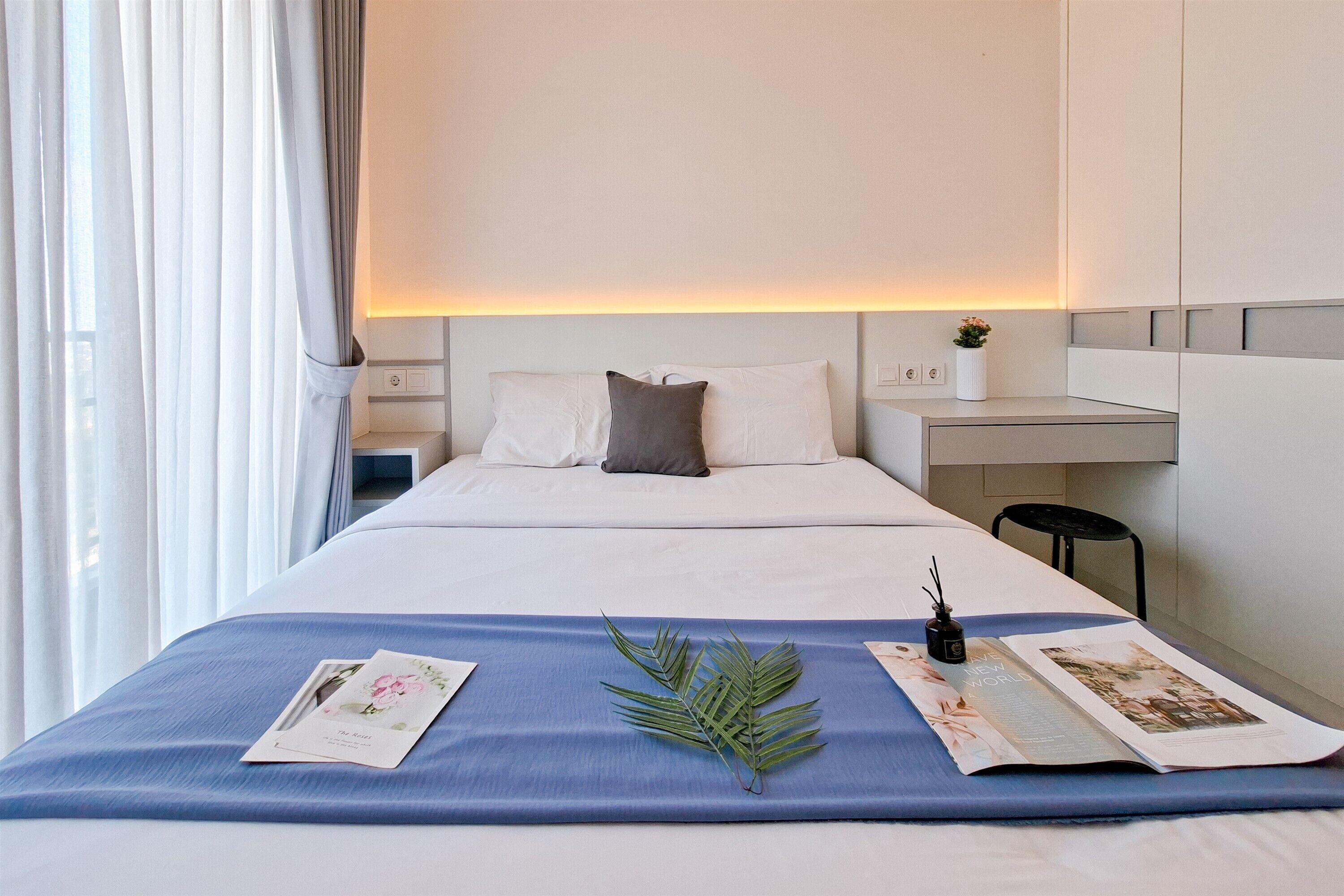 Ein Hotelzimmer mit einem ordentlich bezogenem Bett, einem Nachttisch mit Lampe, einer kleinen Pflanze und einer Zeitschrift auf dem Bett.