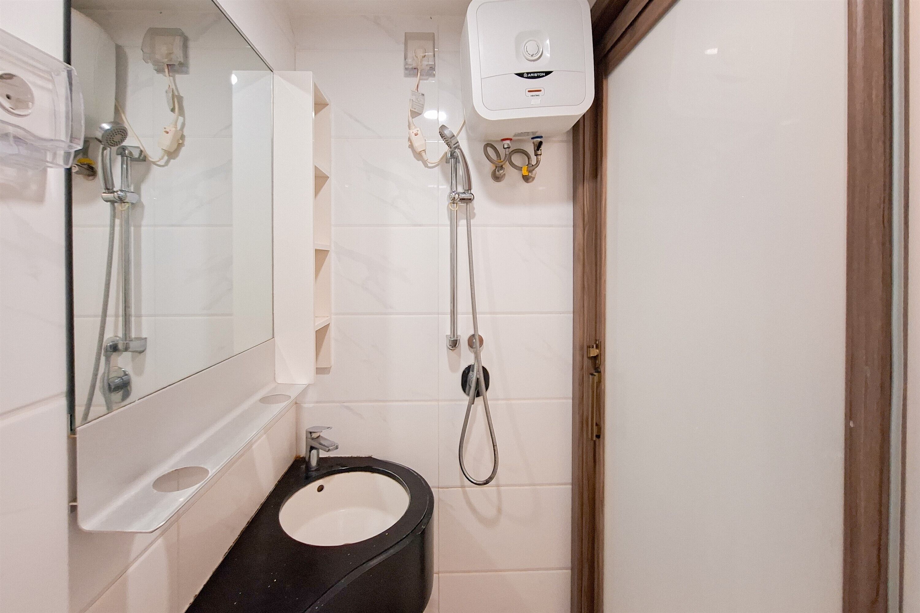 Une salle de bain avec un lavabo noir, un miroir, une douchette à main et un robinet fixé au mur.