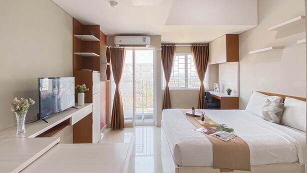 A modern hotel room with a bed, a desk, a TV, and a window with curtains. - Minimalist Style Studio At Royal Sentul Park Apartment (Bogor)