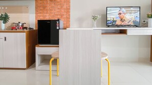 A modern kitchen with a brick wall, a built-in hexagonal shelf, a refrigerator, a stove, and a dining area with yellow chairs. - Minimalist Style Studio At Royal Sentul Park Apartment (Bogor)