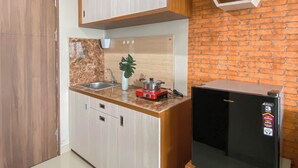 A compact kitchen with wooden cabinets, a marble countertop, a sink, a small plant, a red appliance, and a black refrigerator. - Minimalist Style Studio At Royal Sentul Park Apartment (Bogor)