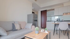 A modern living room with a sofa, a coffee table, and a small kitchen area with a refrigerator, microwave, and dining table. - Solace 2Br Near Cikini Station At Menteng Park Apartment (Jakarta)