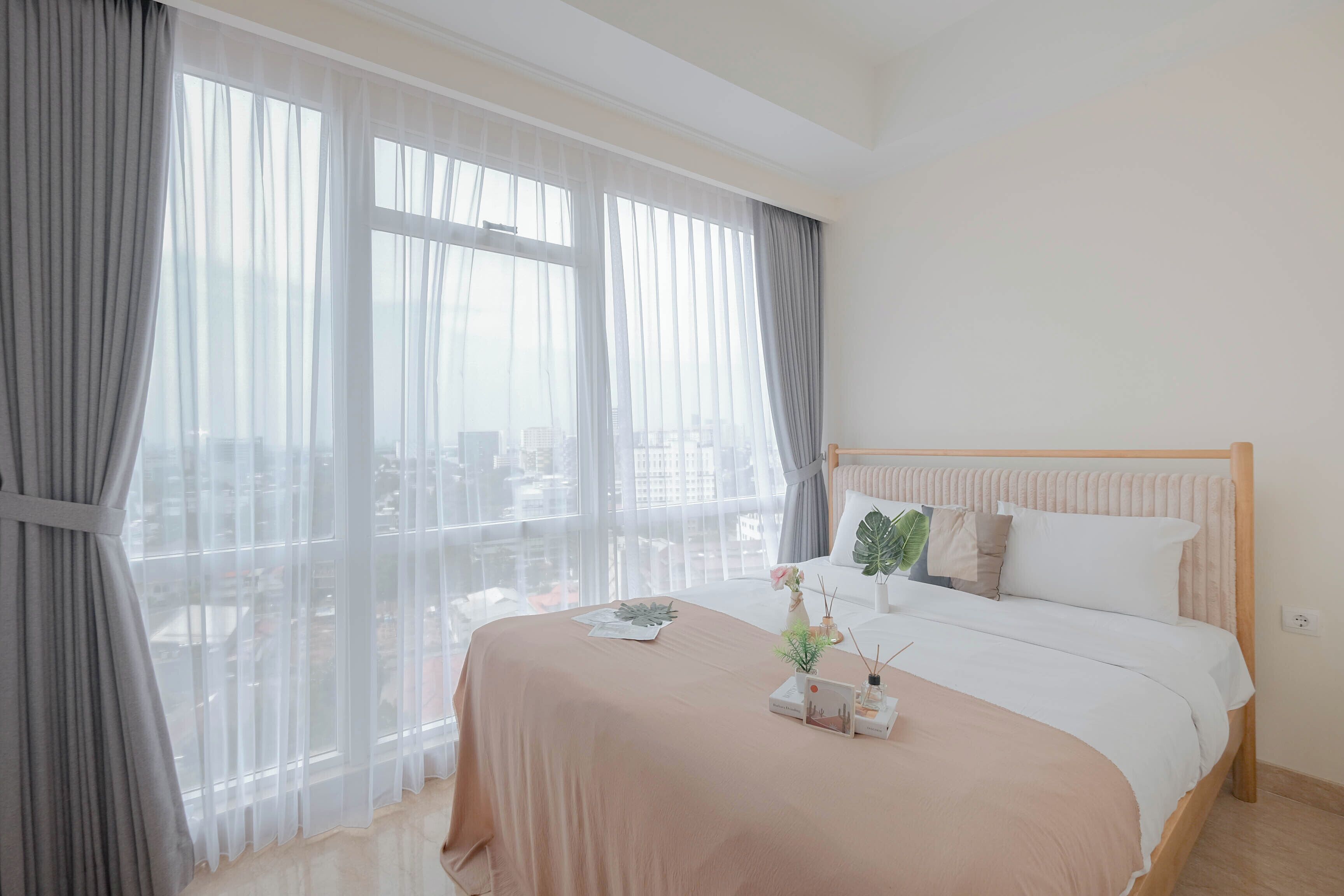 A modern hotel room with a large window, a bed with a wooden headboard, and a city view.