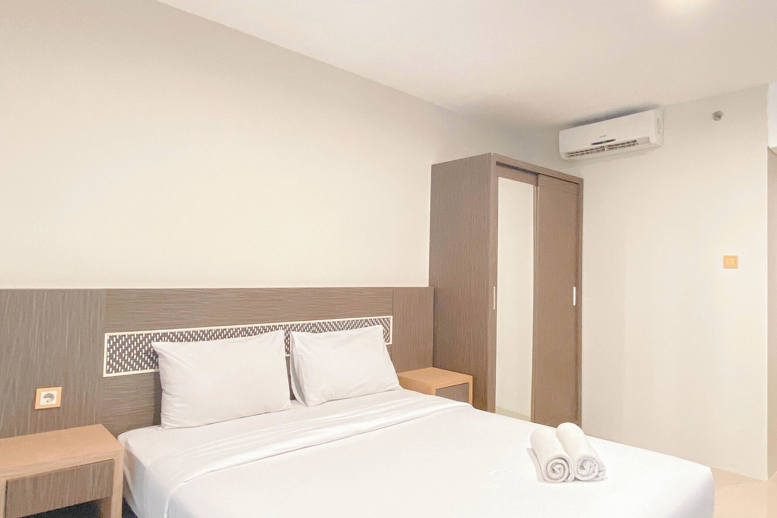 A hotel room with a bed, nightstands, a wardrobe, and an air conditioning unit.