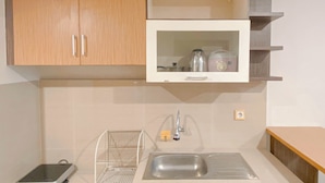 A kitchen with wooden cabinets, a built-in microwave, a sink, and a small shelf. - Studio Room Near Mall At Star Semarang Apartment (Semarang)