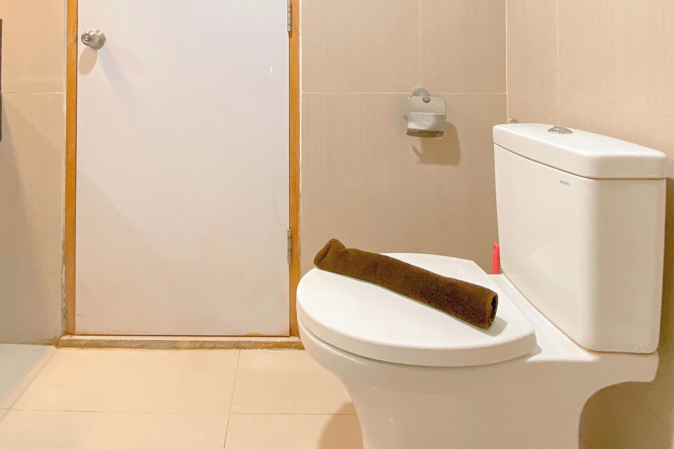 A white toilet with a brown towel on the seat, a flush handle, and a small shelf with a tissue holder.