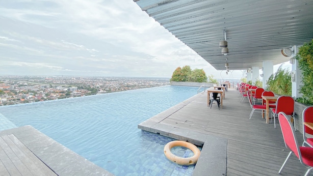 An infinity pool with a view of a cityscape, red chairs, and a wooden deck. - Studio Room Near Mall At Star Semarang Apartment (Semarang)