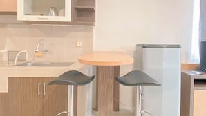 A compact kitchen with a sink, a microwave, a refrigerator, and two bar stools. - Studio Room Near Mall At Star Semarang Apartment (Semarang)