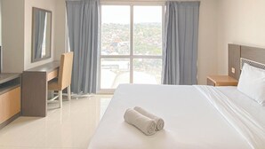 A hotel room with a bed, a desk, a chair, and a large window with curtains. - Studio Room Near Mall At Star Semarang Apartment (Semarang)