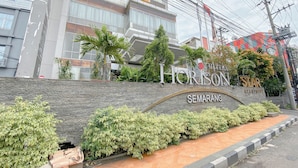 A hotel entrance with a stone wall, greenery, and a sign reading "Horizon Semarang". - Studio Room Near Mall At Star Semarang Apartment (Semarang)