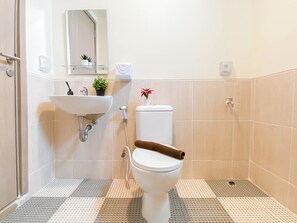 Een badkamer met een witte wasbak, toilet en douche. Er staan potplanten op de wasbak en er ligt een handdoek op het toilet. De vloer heeft een patroon van tegels.