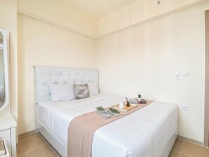 Een net opgemaakt bed met een wit hoofdeinde en een beige plaid. Er staat een kleine plant en een boek op het bed.