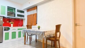 A compact kitchen with green cabinets, a red backsplash, and a dining table with a white tablecloth. - Simple 2Br Near Industrial Area Apartment Meikarta (Cikarang)