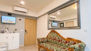 A room with a wooden door, a sofa with a floral pattern, a large mirror, and a television on the wall. - Simple 2Br Near Industrial Area Apartment Meikarta (Cikarang)