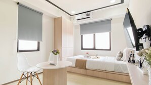 A modern hotel room with a bed, a small round table, a chair, and a desk with a computer monitor. - White Accent Studio At Apartment Meikarta Near Paramadina University (Cikarang)