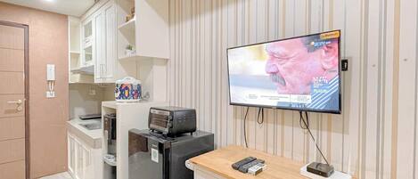 A modern kitchen with a built-in microwave, toaster, and refrigerator. A flat-screen TV mounted on the wall displays a sports event.