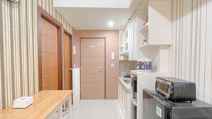 A compact kitchen with a wooden table, a refrigerator, and a microwave. - 2Br Near Panakkukang Mall At Apartment Vida View Makassar (Makassar)