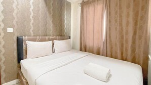 A neatly made bed with white linens and a rolled towel, a headboard, and curtains. - 2Br Near Panakkukang Mall At Apartment Vida View Makassar (Makassar)