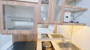 A compact kitchenette with a sink, stove, and a microwave. - Basic Studio At Candiland Apartment (Semarang)