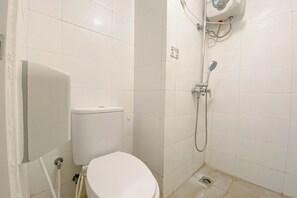A small, white-tiled bathroom with a toilet, a shower, and a toilet paper holder. - Basic Studio At Candiland Apartment (Semarang)