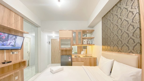 A hotel room with a bed, a television, a kitchenette, and a bathroom. - Basic Studio At Candiland Apartment (Semarang)