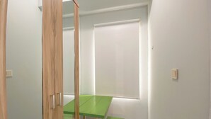 A room with a green table and two matching chairs, a wooden door, and a window with a white blind. - Basic Studio At Candiland Apartment (Semarang)