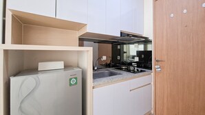 A compact kitchen with white cabinets, a built-in stove, and a refrigerator. - Comfy And Functional Studio At Apartment B Residence (Pagedangan)