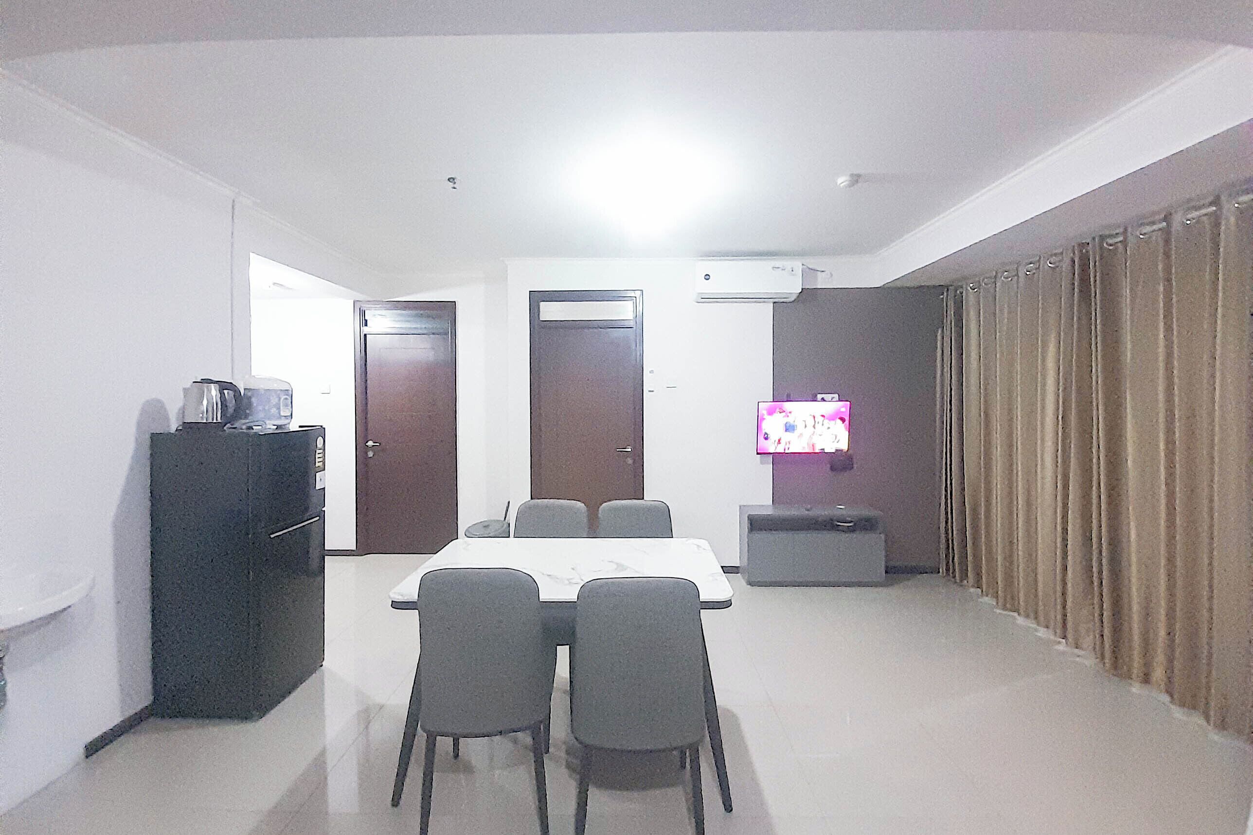 A room with a dining table, four chairs, a television, a refrigerator, and a door.