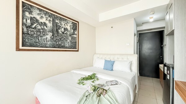 Un dormitorio con una cama, un cuadro blanco y negro enmarcado, y una puerta que da a un baño.