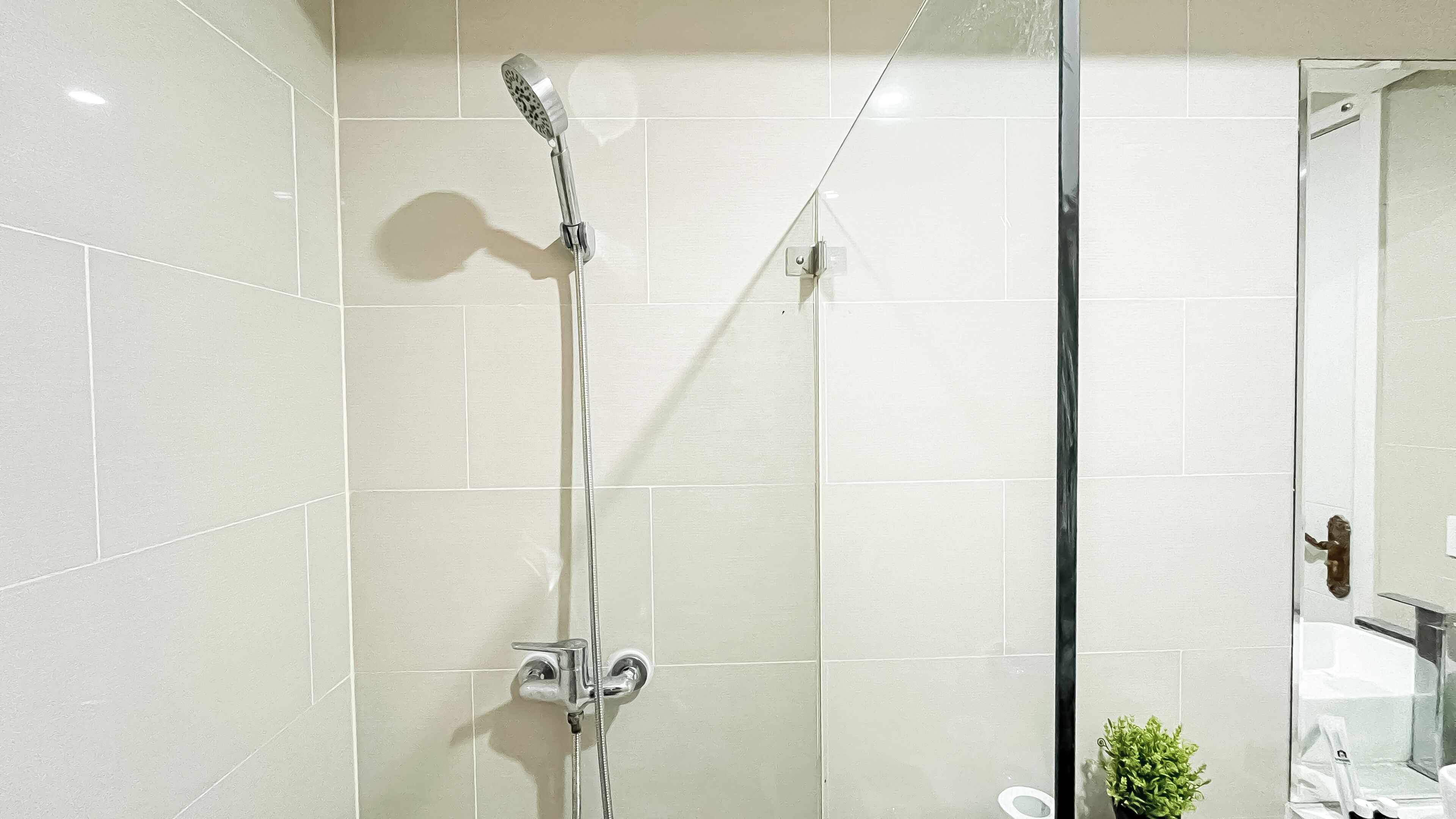 A modern bathroom with a glass shower enclosure, white tiles, and a small potted plant.
