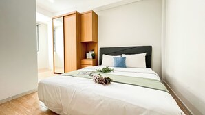 A bedroom with a bed, a wooden wardrobe, a nightstand, and a window. - Serene Stay 2Br At Daan Mogot City Apartment (Jakarta)