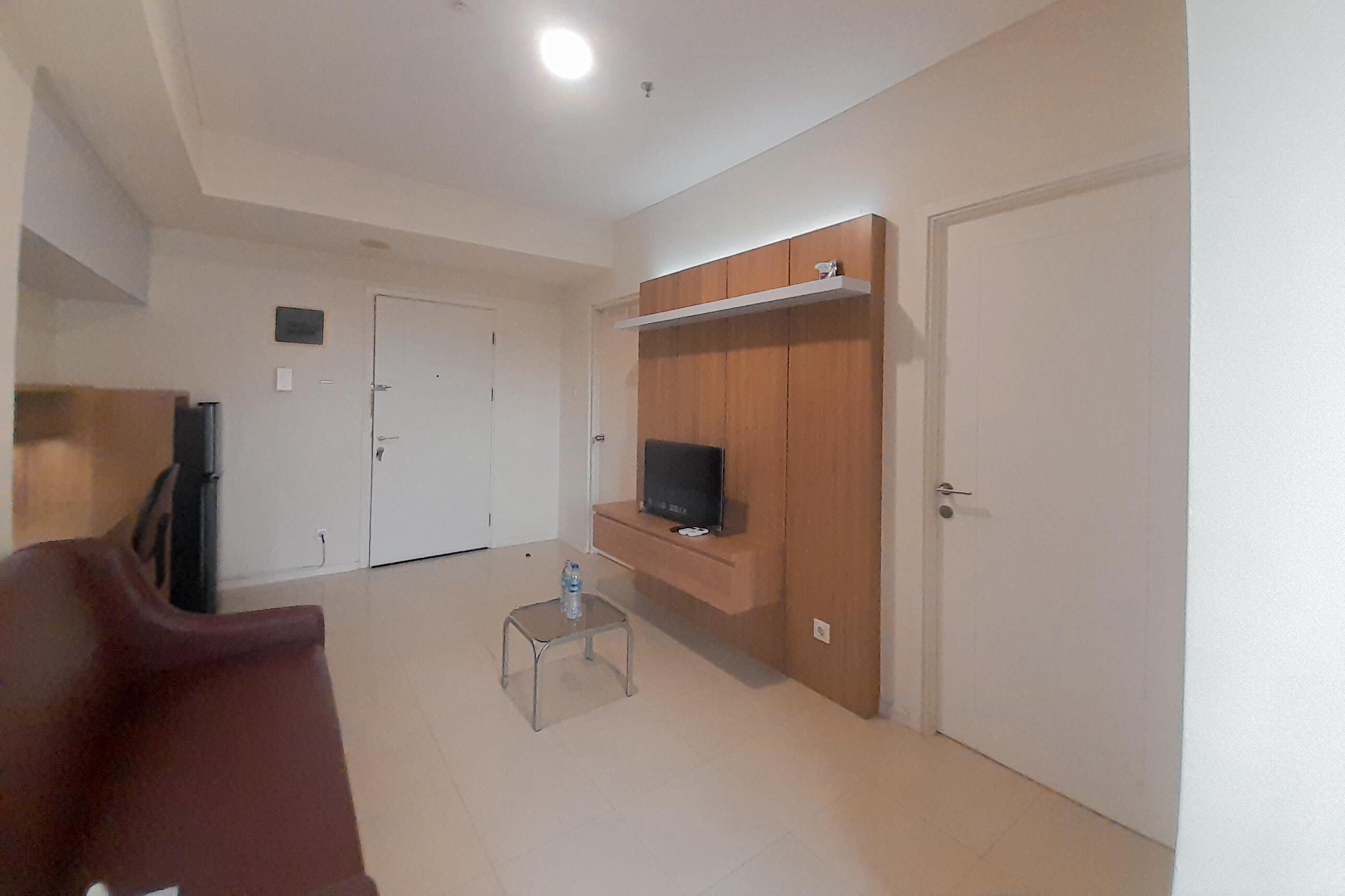 Una sala de estar moderna con un televisor sobre un mueble de madera, una mesita con una botella de agua y una silla roja.