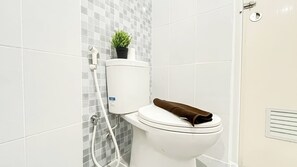 A modern bathroom with a toilet, a shower, and a small potted plant on the wall. - Simple Designed 2Br Near Tokyo Hub At Tokyo Riverside Pik 2 Apartment (Teluknaga)