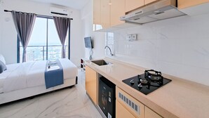 Una habitación de hotel moderna con una cama, una cocina con estufa, un lavabo y una ventana con cortinas.