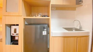 A compact kitchen with wooden cabinets, a stainless steel refrigerator, a built-in coffee machine, and a white sink. - Wooden Nest Studio At The Alton Apartment (Semarang)