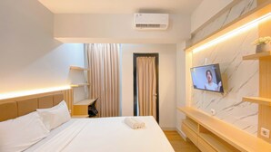 A hotel room with a bed, a TV mounted on the wall, a desk, and a window with curtains. - Wooden Nest Studio At The Alton Apartment (Semarang)