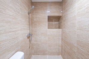 Un petit espace de douche carrelé, équipé d’un pommeau de douche à main et d’un robinet fixé au mur.