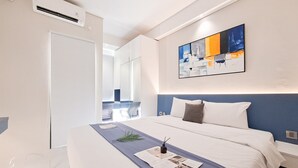 Moderni hotellihuone, jossa on suuri sänky, yöpöytä, seinälle asennettu ilmastointilaite ja ikkuna, josta on näkymä ulos.